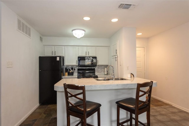 kitchen with sink, a kitchen breakfast bar, decorative backsplash, white cabinets, and black appliances