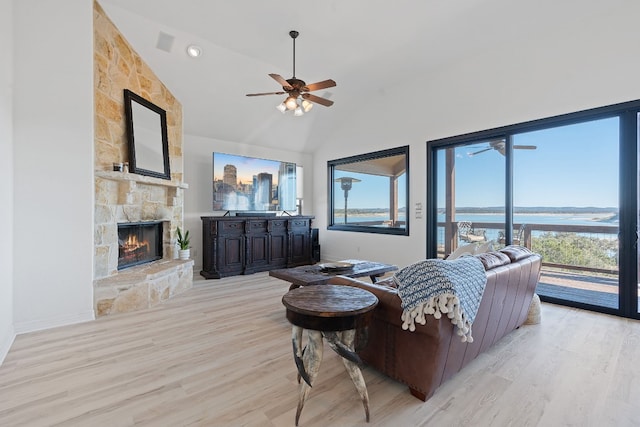 living room with ceiling fan, light hardwood / wood-style floors, vaulted ceiling, a fireplace, and a water view