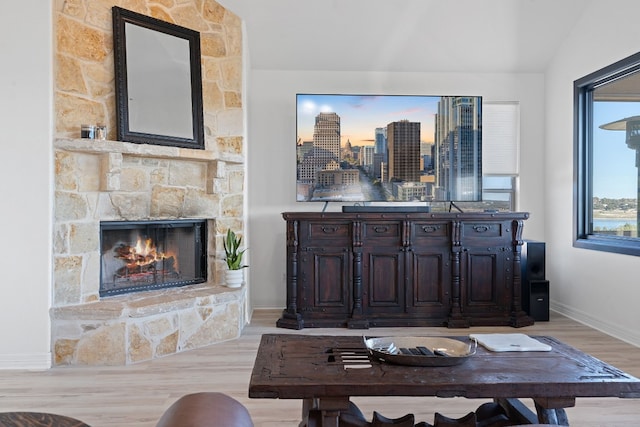 living room with vaulted ceiling, light hardwood / wood-style flooring, and a stone fireplace