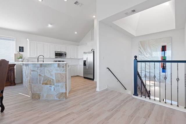 kitchen featuring white cabinetry, sink, stainless steel appliances, light hardwood / wood-style flooring, and high vaulted ceiling