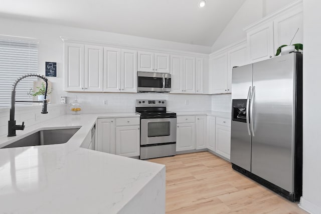 kitchen featuring light stone countertops, stainless steel appliances, vaulted ceiling, sink, and white cabinetry