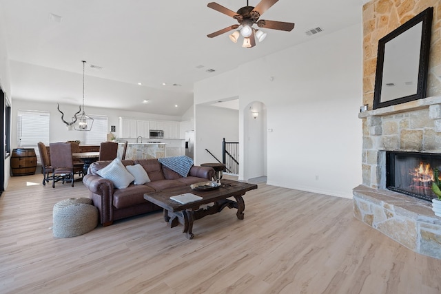 living room featuring a stone fireplace, light hardwood / wood-style flooring, ceiling fan with notable chandelier, and lofted ceiling