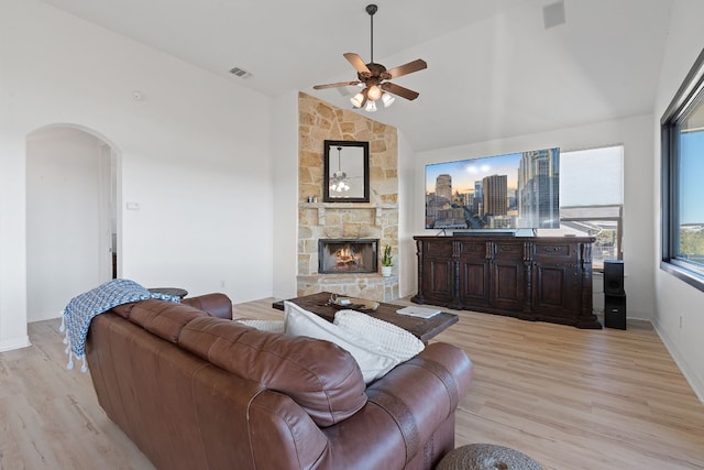 living room with a stone fireplace, ceiling fan, light hardwood / wood-style floors, and lofted ceiling