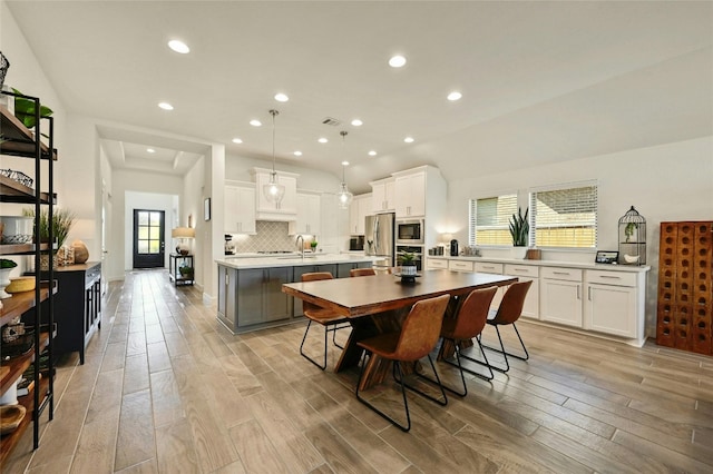 kitchen with a kitchen bar, stainless steel appliances, a kitchen island with sink, pendant lighting, and white cabinetry