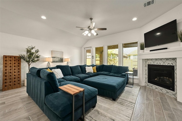 living room with ceiling fan, lofted ceiling, and a tile fireplace