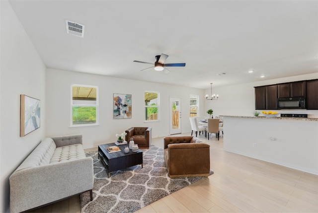 living room with light hardwood / wood-style floors and ceiling fan with notable chandelier