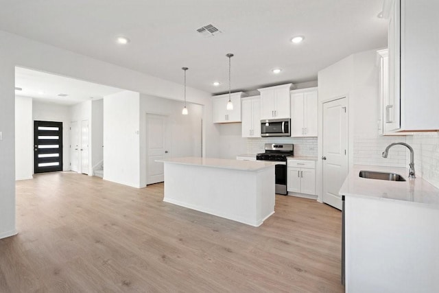 kitchen featuring sink, white cabinetry, appliances with stainless steel finishes, a kitchen island, and light hardwood / wood-style floors