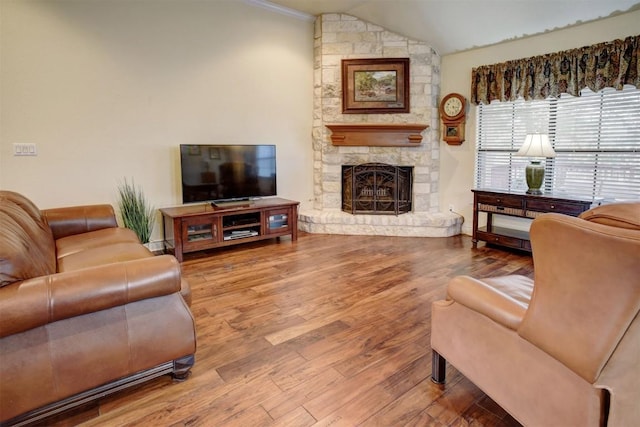 living room with wood-type flooring, a stone fireplace, and lofted ceiling