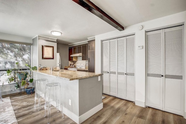 kitchen with light stone countertops, a kitchen breakfast bar, dark brown cabinetry, white range with electric stovetop, and beamed ceiling