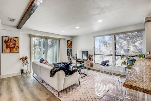 living room featuring beamed ceiling, plenty of natural light, light hardwood / wood-style floors, and a textured ceiling