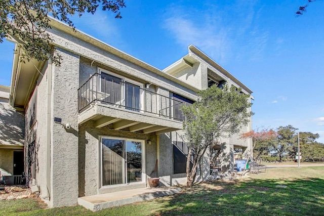 back of house with a lawn and a balcony