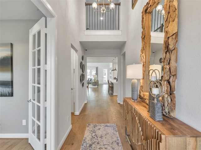 foyer with a towering ceiling, an inviting chandelier, french doors, and light wood-type flooring