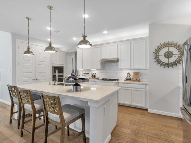 kitchen with light hardwood / wood-style floors, white cabinetry, a kitchen island with sink, and hanging light fixtures