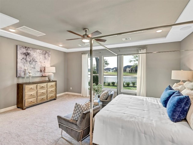 bedroom featuring light carpet, a tray ceiling, ceiling fan, and a water view