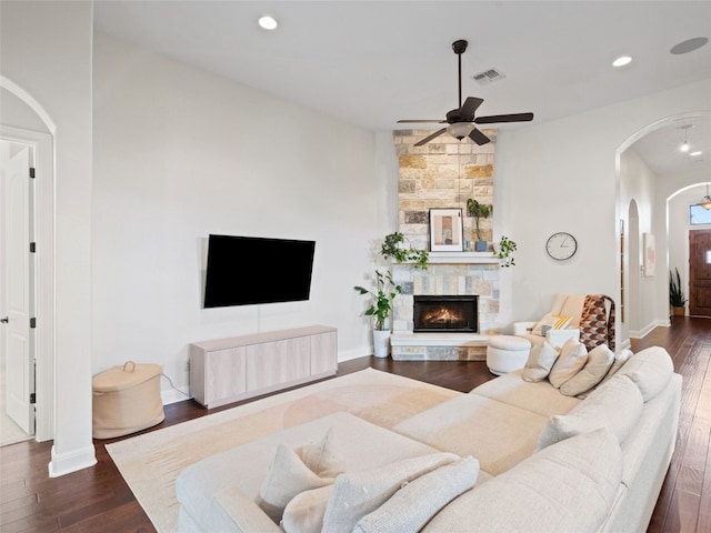 living room featuring ceiling fan, a stone fireplace, and dark hardwood / wood-style flooring