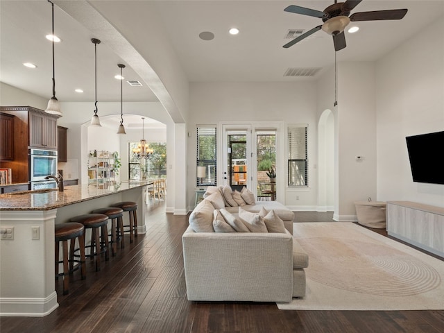 living room with ceiling fan with notable chandelier, dark wood-type flooring, and sink