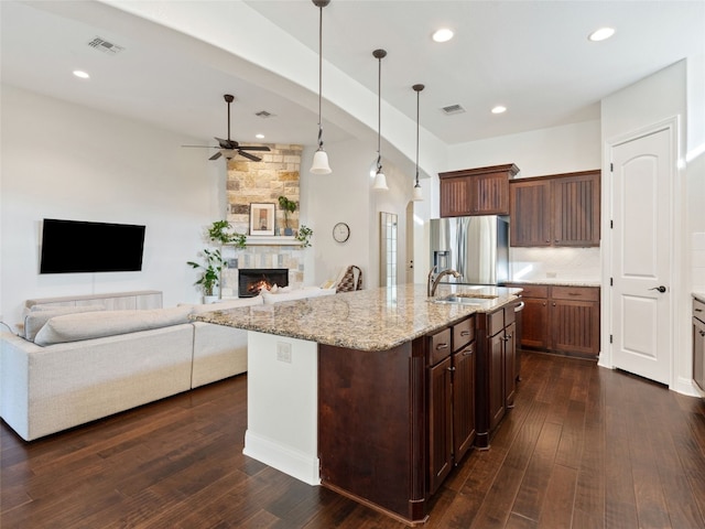 kitchen featuring stainless steel fridge, ceiling fan, pendant lighting, a center island with sink, and a fireplace