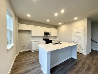 kitchen with light countertops, appliances with stainless steel finishes, an island with sink, and white cabinetry