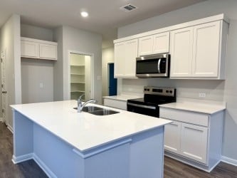 kitchen with an island with sink, stainless steel appliances, dark wood-style floors, white cabinetry, and a sink