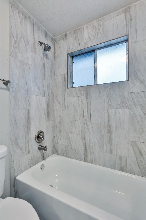 bathroom with tiled shower / bath combo and toilet