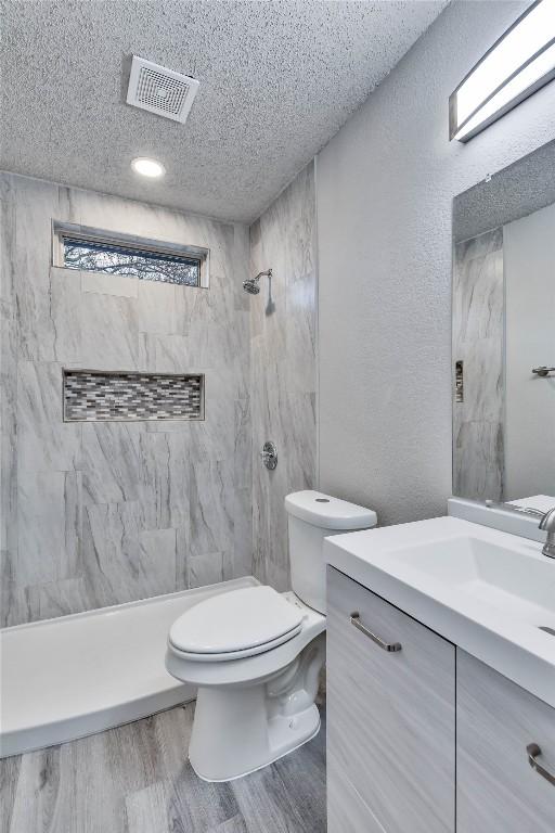 bathroom featuring a tile shower, a textured ceiling, vanity, hardwood / wood-style floors, and toilet