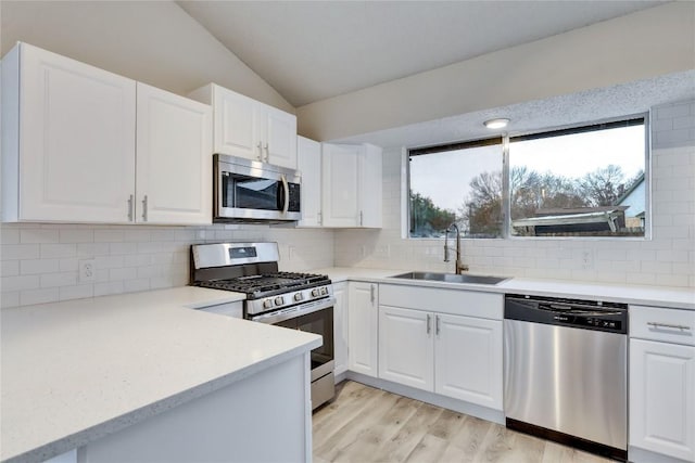 kitchen featuring sink, vaulted ceiling, tasteful backsplash, white cabinetry, and stainless steel appliances