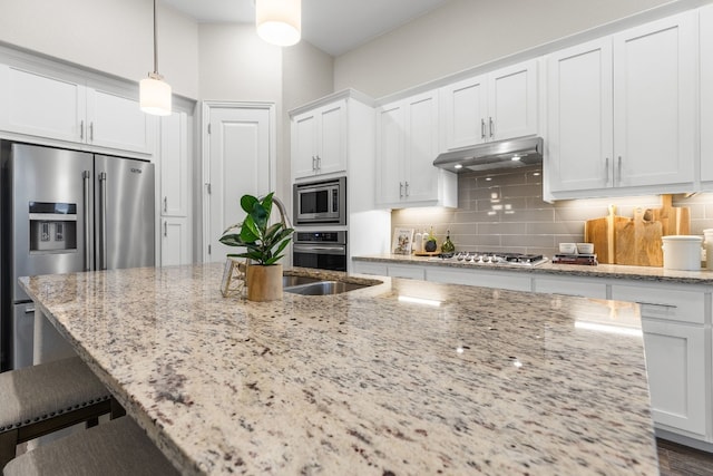 kitchen with light stone countertops, white cabinets, decorative light fixtures, and appliances with stainless steel finishes