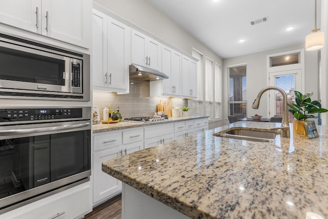 kitchen featuring white cabinetry, light stone countertops, sink, decorative light fixtures, and appliances with stainless steel finishes