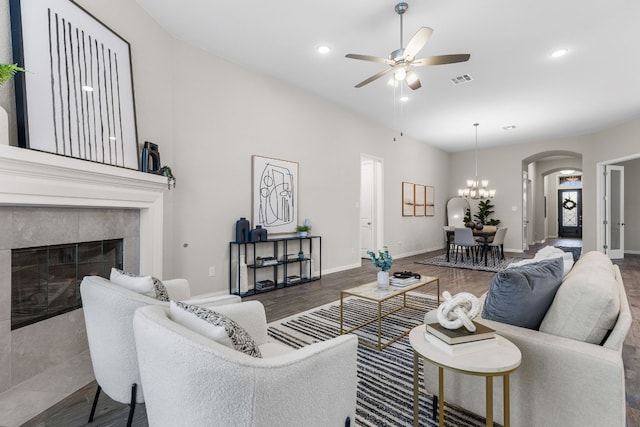 living room with ceiling fan with notable chandelier, dark wood-type flooring, and a tile fireplace