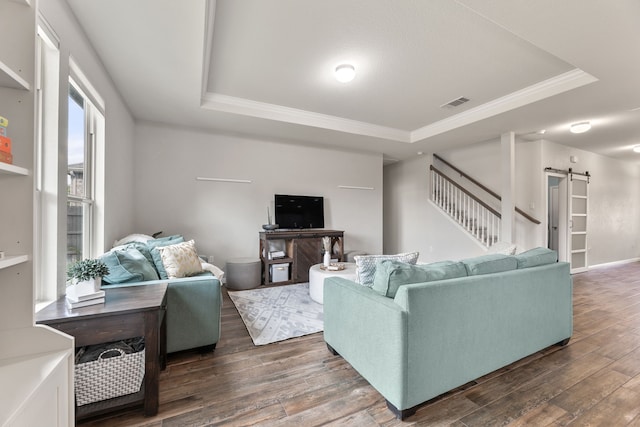 living room with a raised ceiling, ornamental molding, a barn door, and dark hardwood / wood-style floors