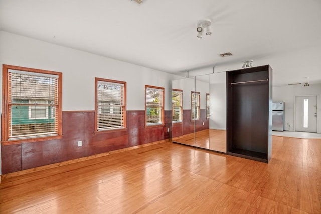 unfurnished bedroom with stainless steel fridge and hardwood / wood-style flooring