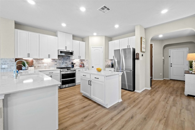 kitchen with light stone counters, stainless steel appliances, sink, white cabinetry, and a kitchen island