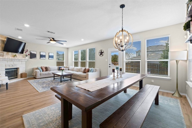 dining area with a fireplace, ceiling fan with notable chandelier, and light hardwood / wood-style flooring