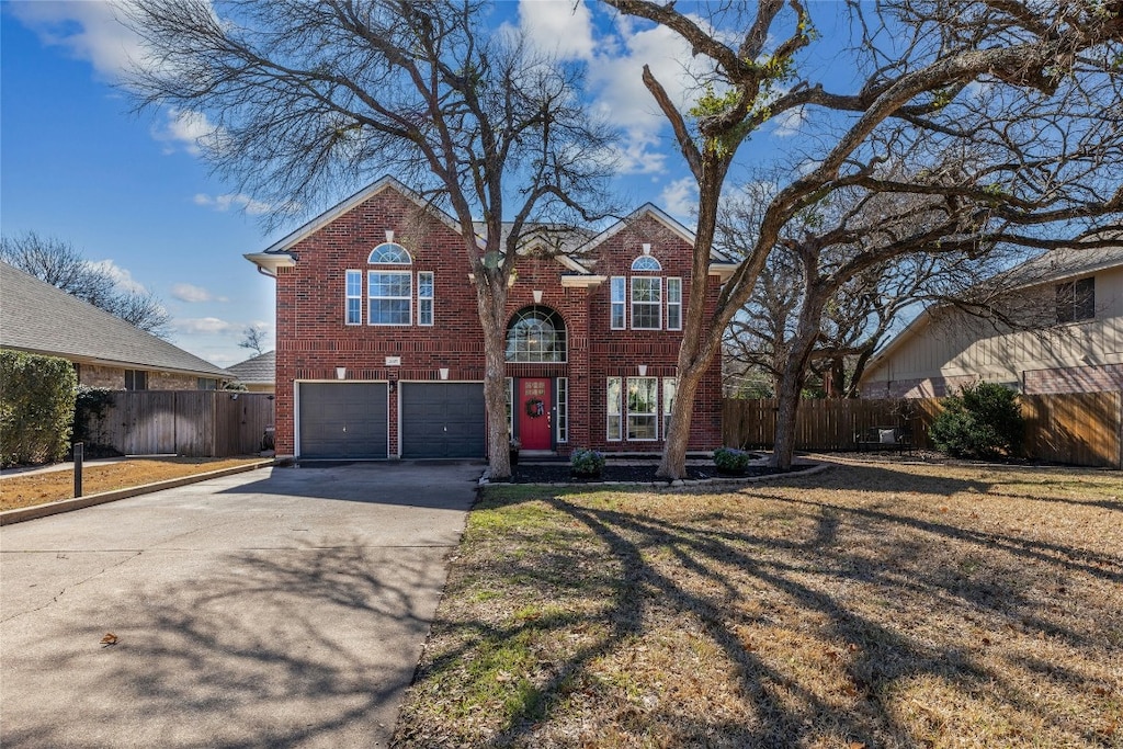 traditional-style home featuring brick siding, an attached garage, fence, driveway, and a front lawn