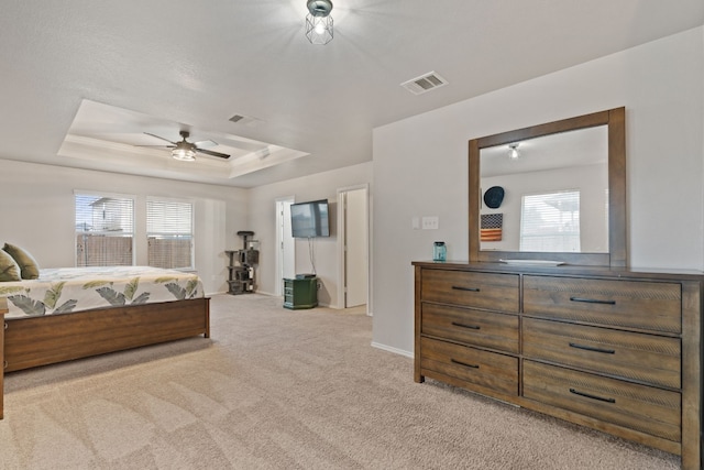 bedroom with multiple windows, light colored carpet, a raised ceiling, and ceiling fan