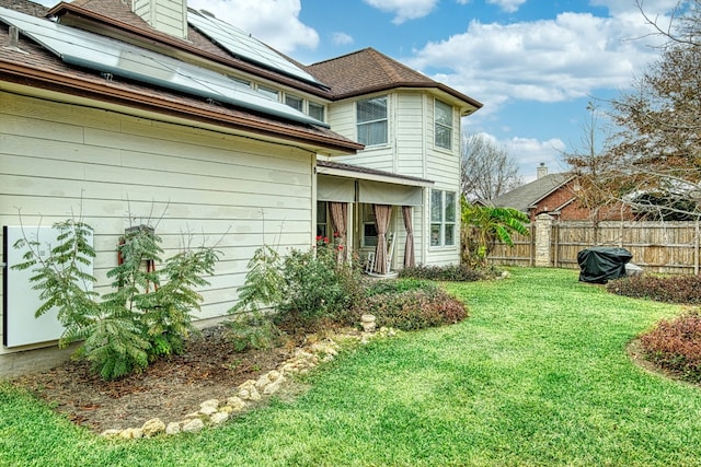 rear view of property featuring a yard and solar panels