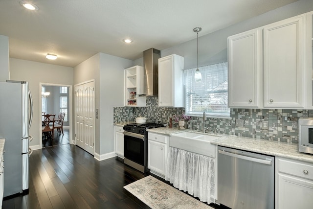 kitchen with light stone countertops, stainless steel appliances, wall chimney range hood, pendant lighting, and white cabinets