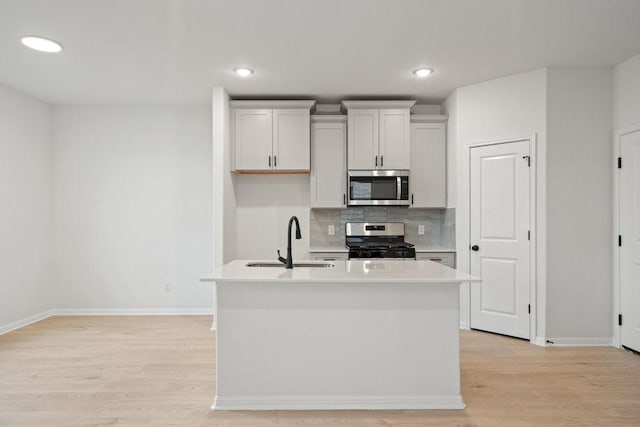 kitchen with sink, light hardwood / wood-style floors, a center island with sink, white cabinets, and appliances with stainless steel finishes