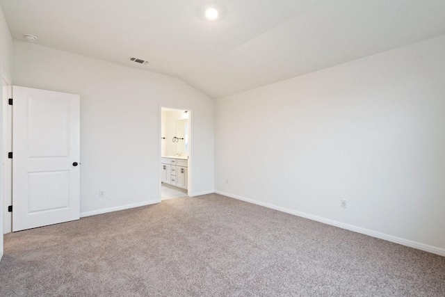 unfurnished bedroom featuring ensuite bathroom, light colored carpet, and vaulted ceiling