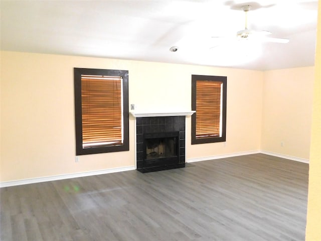 unfurnished living room with a tile fireplace, ceiling fan, and dark wood-type flooring