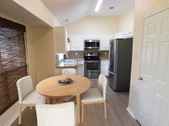 dining space featuring wood-type flooring, sink, and vaulted ceiling