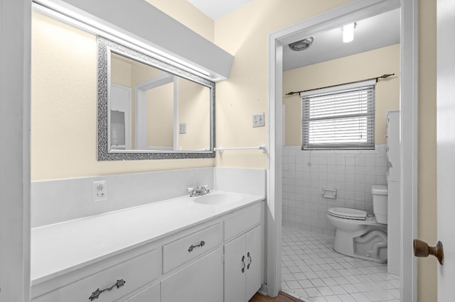 bathroom with toilet, vanity, tile patterned floors, and tile walls