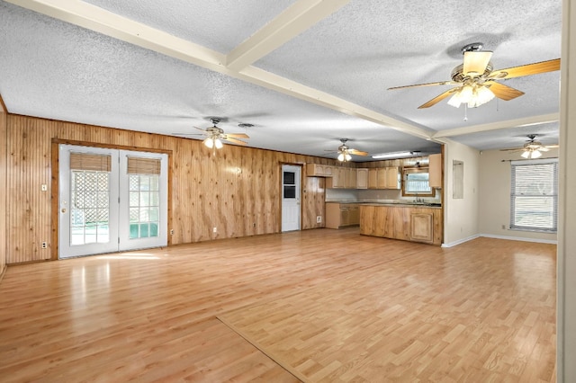 unfurnished living room featuring wood walls, beam ceiling, a textured ceiling, and a wealth of natural light