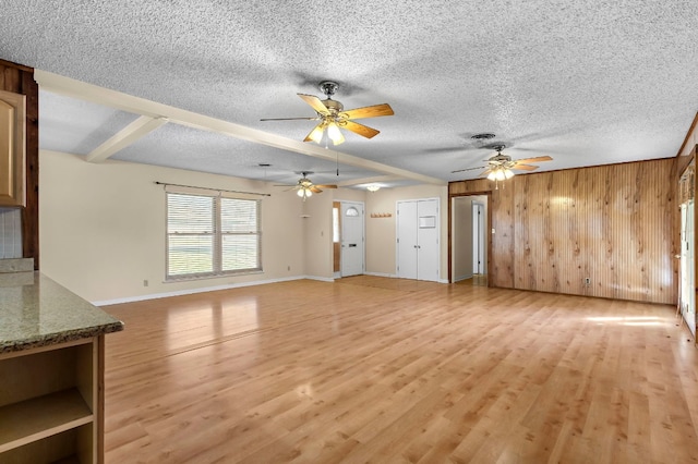 unfurnished living room with wooden walls, light hardwood / wood-style flooring, ceiling fan, and a textured ceiling