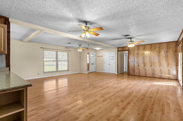 901 Berrywood Dr, Austin, TX 78753 - unfurnished living room featuring light wood-type flooring, wooden walls, a ceiling fan, baseboards, and a textured ceiling