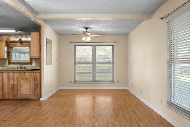 unfurnished dining area with a textured ceiling, ceiling fan, sink, light hardwood / wood-style flooring, and beamed ceiling