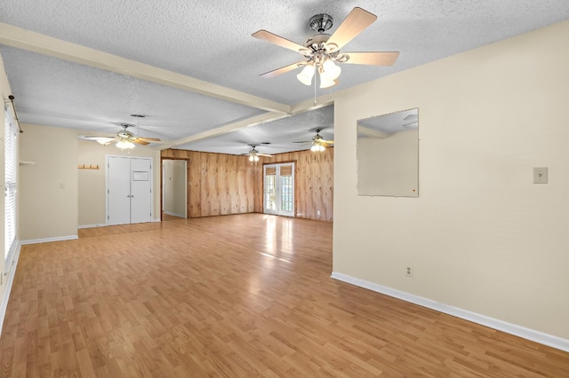 unfurnished living room featuring ceiling fan, wood walls, a textured ceiling, and light hardwood / wood-style flooring