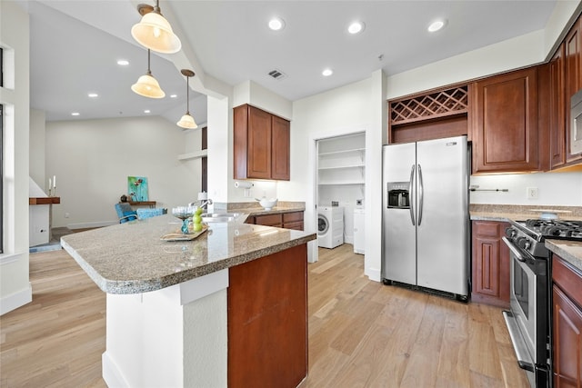 kitchen featuring appliances with stainless steel finishes, washer and dryer, light wood-type flooring, kitchen peninsula, and pendant lighting