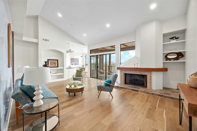 living room featuring high vaulted ceiling, built in shelves, and light hardwood / wood-style flooring