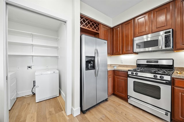 kitchen featuring appliances with stainless steel finishes, light wood-type flooring, washer / clothes dryer, and light stone counters